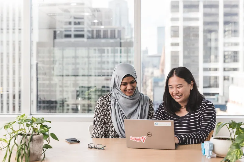 Two women working at a laptop by a window