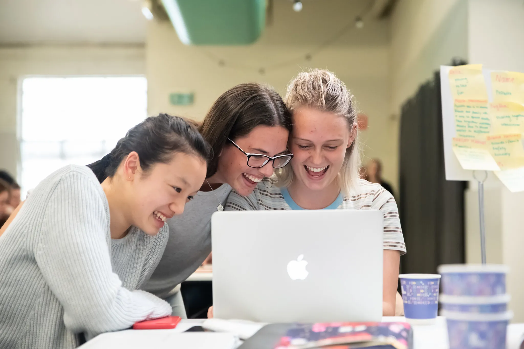 Three women laughing together at a laptop