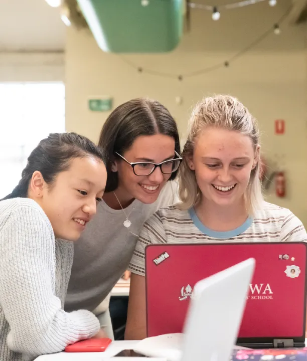 Three young women laughing at a laptop