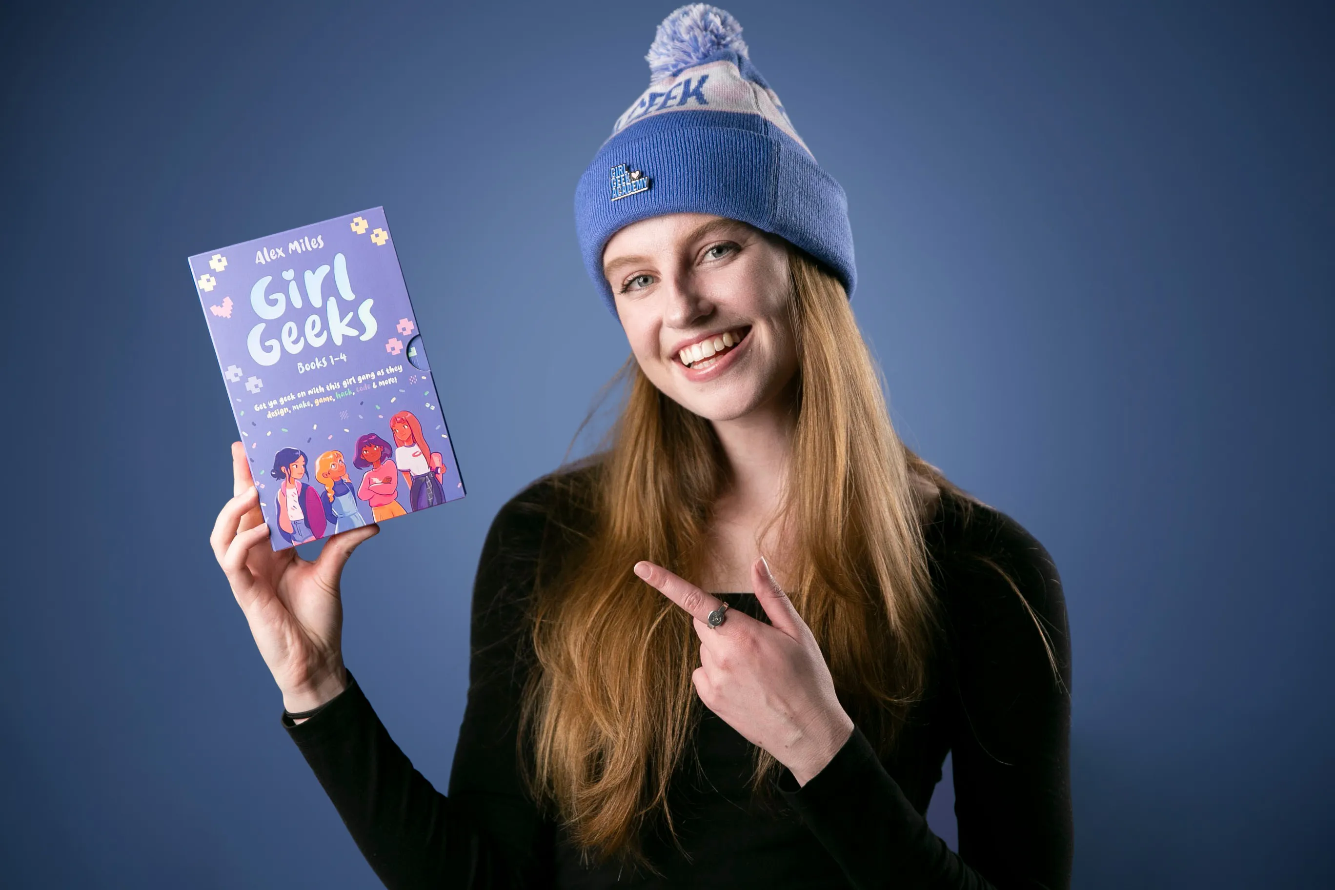 A reader in a Girl Geek Academy beanie pointing to a Girl Geeks book