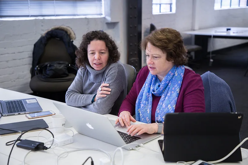Two women working through a problem on a laptop at #SheHacks 2017