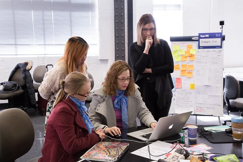 A team at their laptops beside a wall of sticky notes at #SheHacks 2017