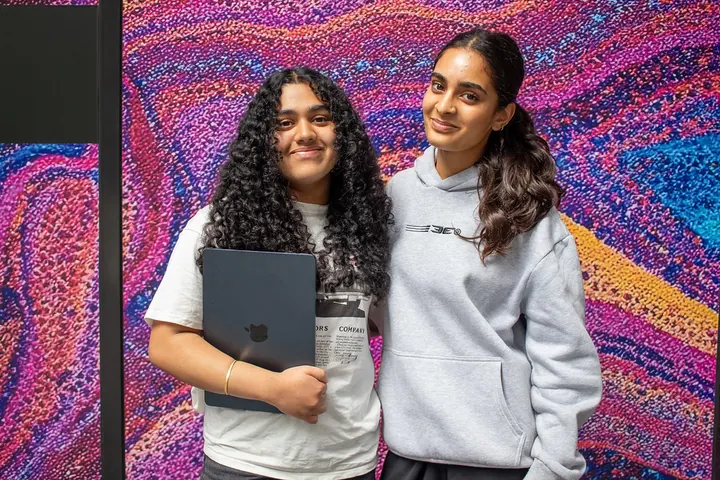 Two students posing in front of a colourful mural