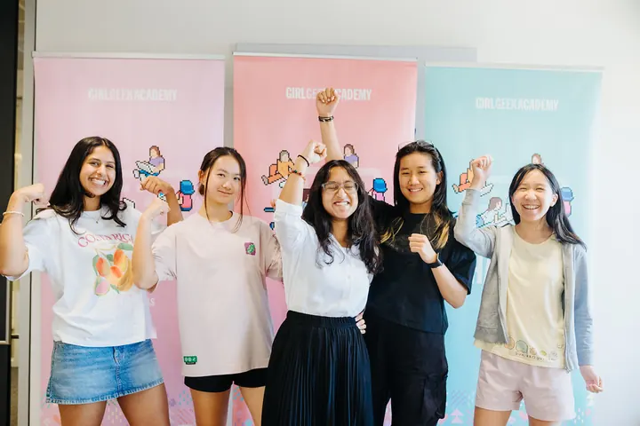Five students flexing in front of Girl Geek Academy banners